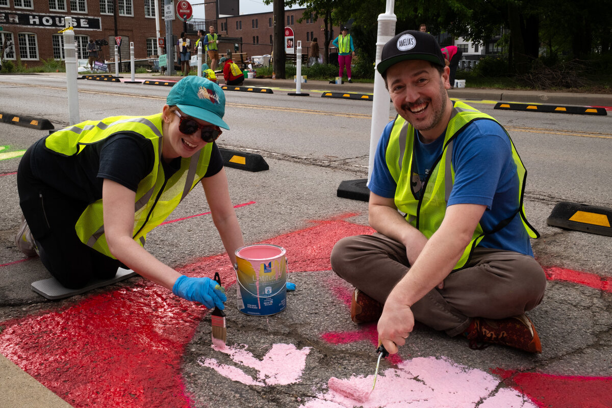 Neighbors in safety vests smiling while painting the street installation
