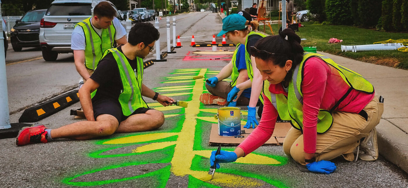 Neighbors in safety vests painting the street together at 16th and Monon